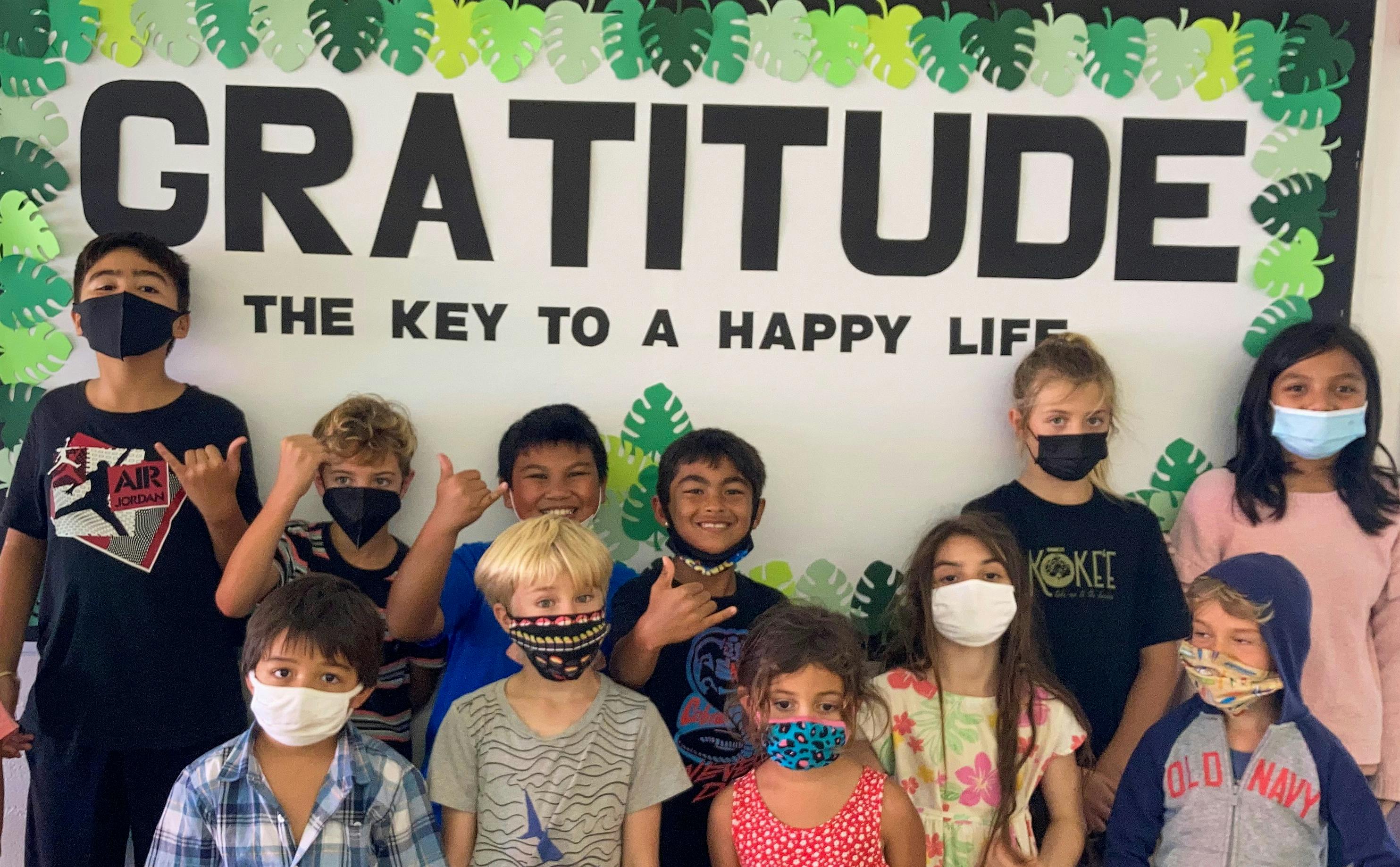 Group of children and teens wearing face masks in front of a sign that says "Gratitude"