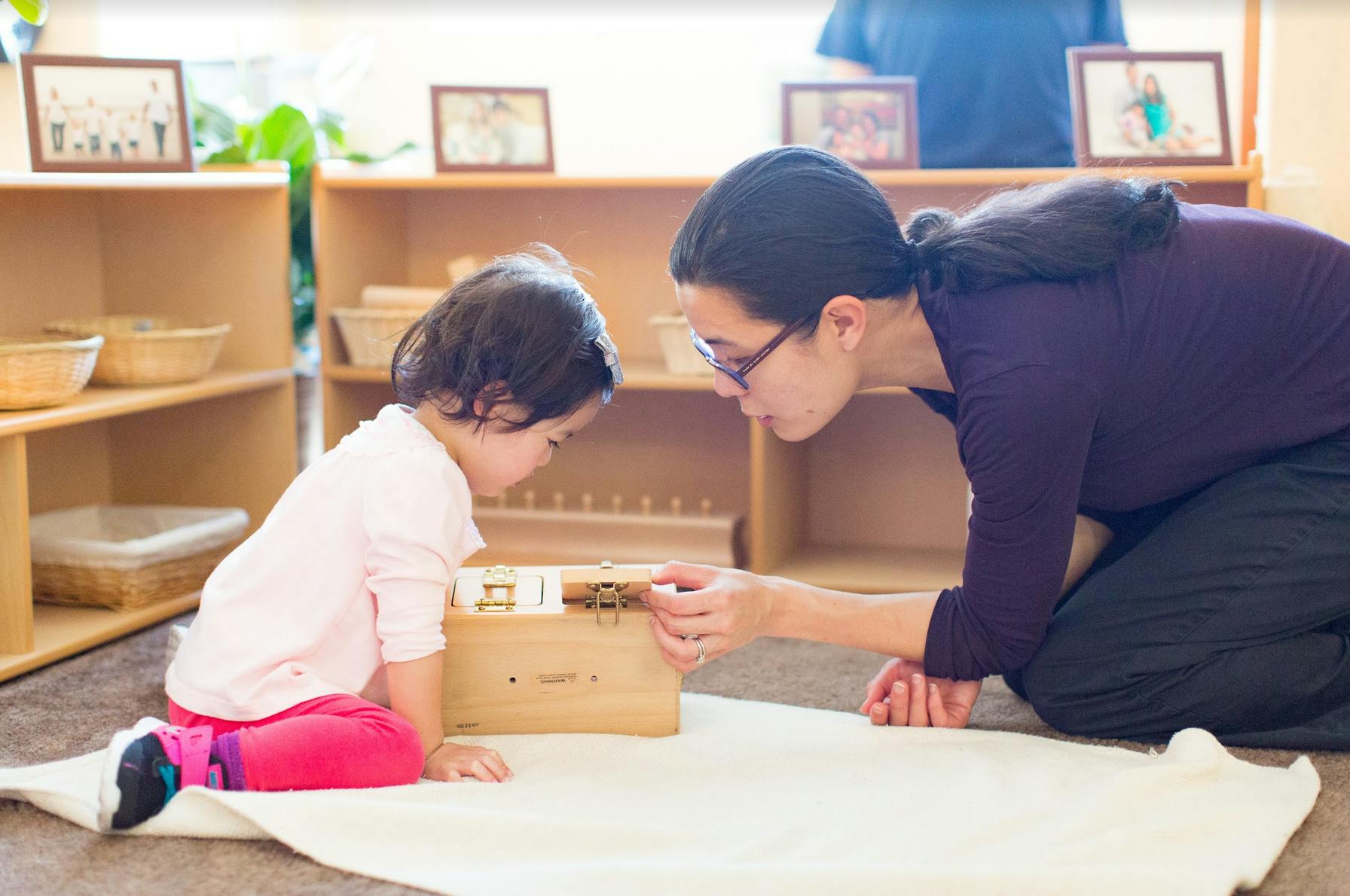 Adult and child kneeling on floor, interacting with a wooden box