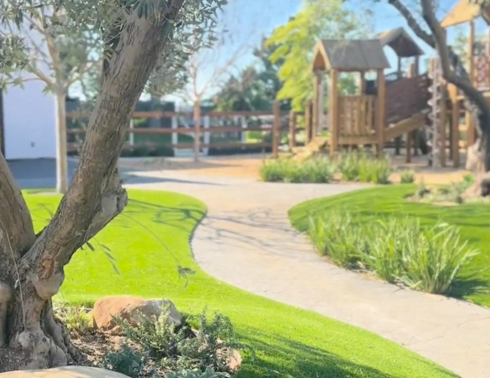 Curved path through green grass with a playground in the background