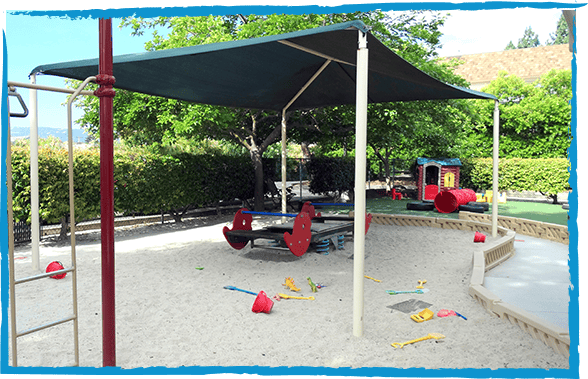 Playground with sand, shade structure, seesaw, and climbing frame