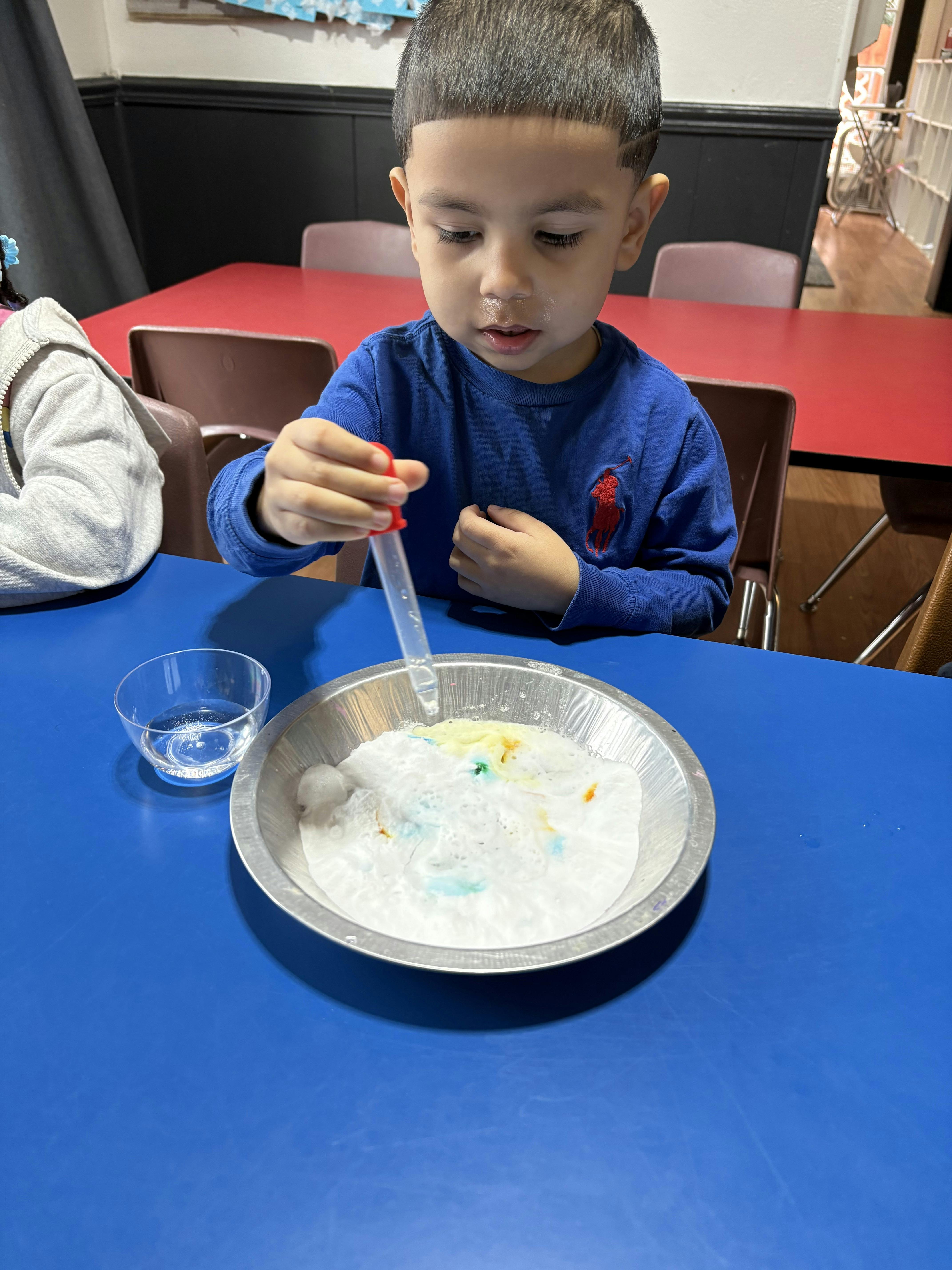 Child using a dropper to add liquid to a foamy substance in a pie tin