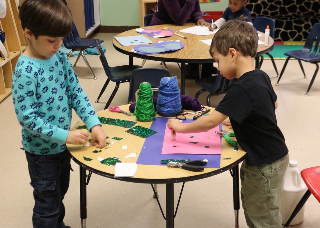Two children doing crafts at a table in a classroom