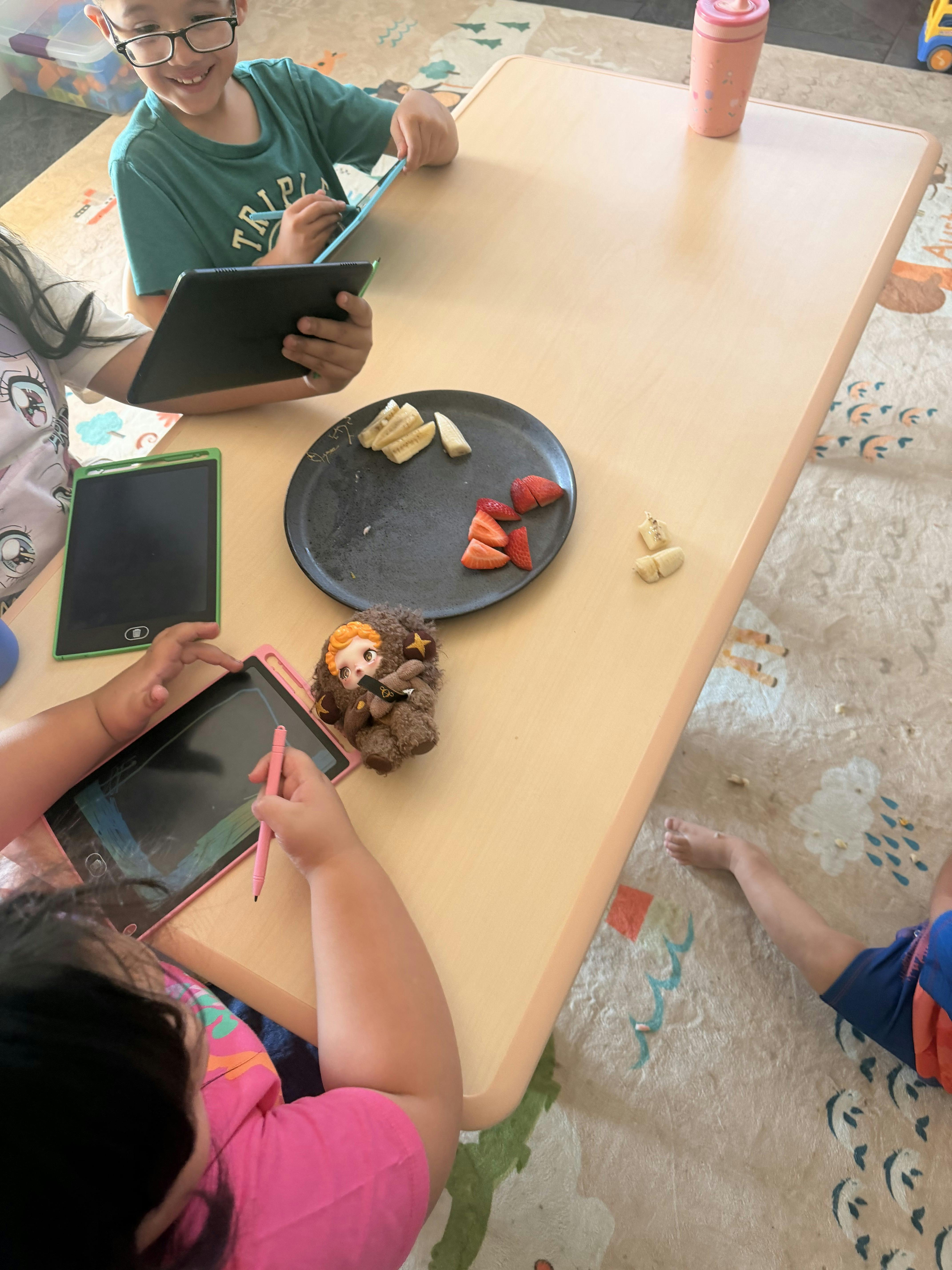 People using writing tablets at a table with fruit