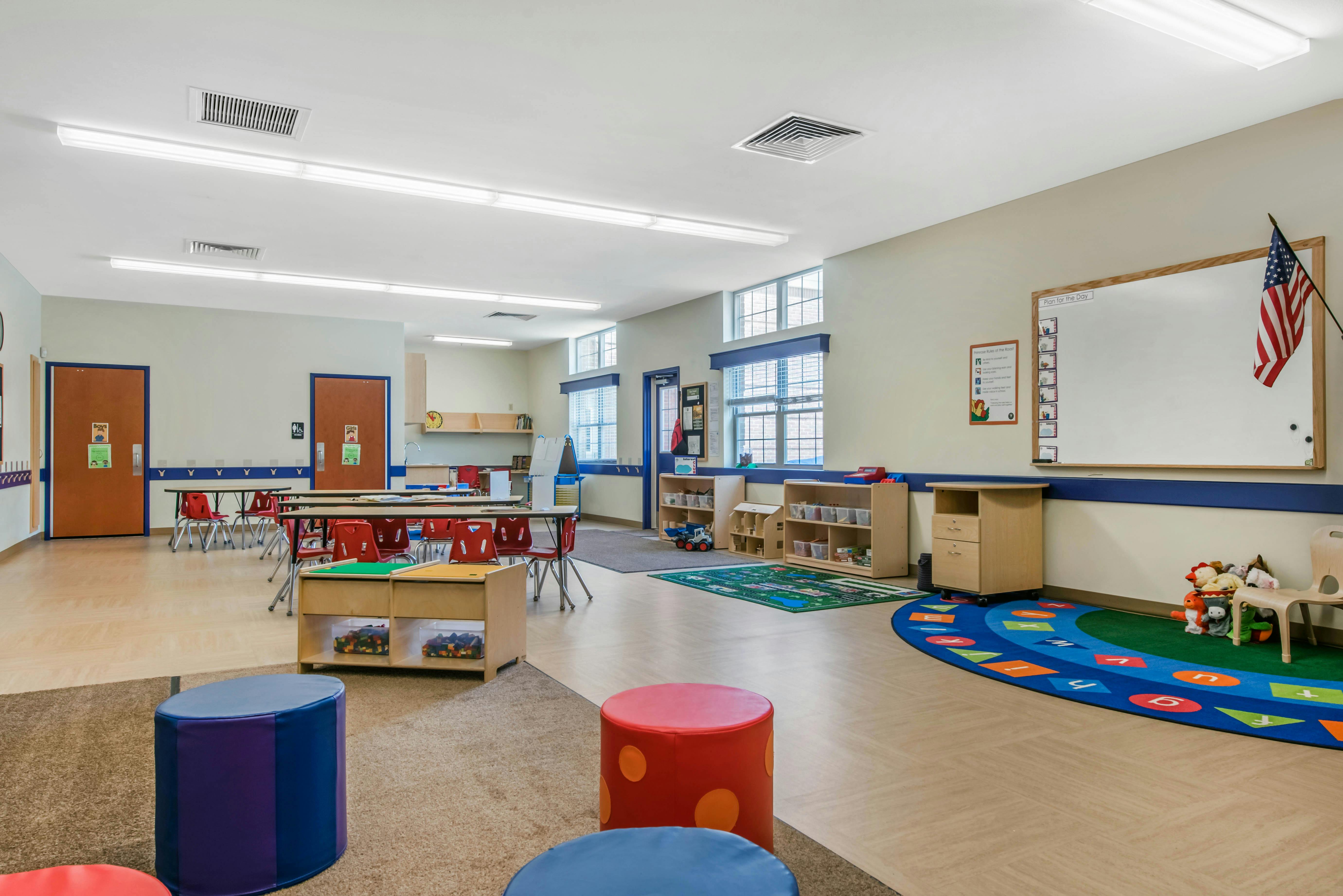 Classroom with tables, chairs, colorful rugs, and play areas