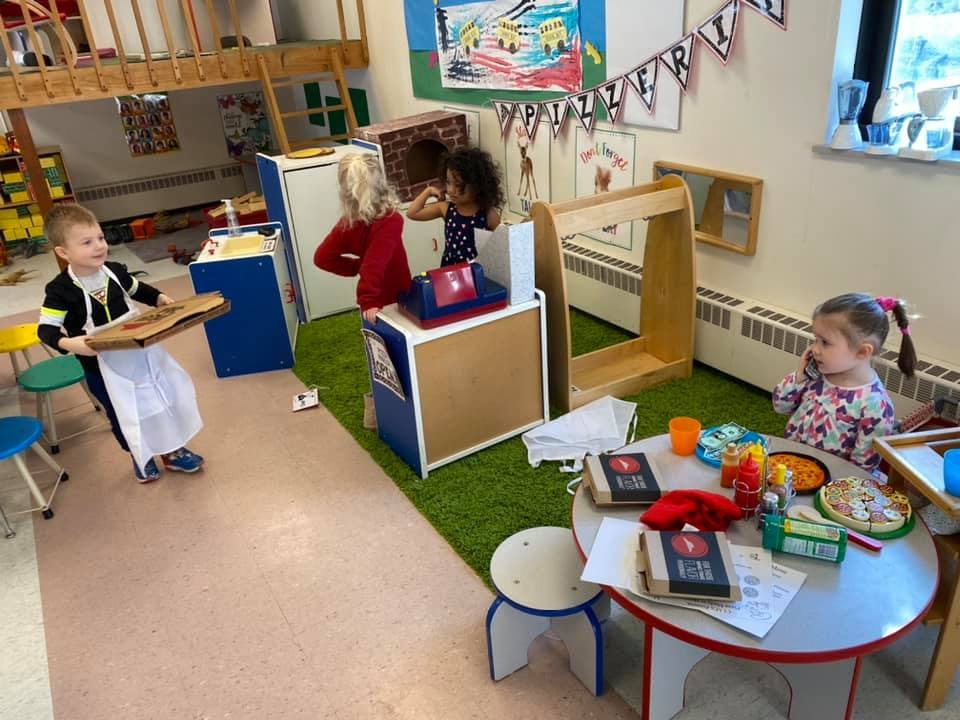 Children playing in a classroom with a child holding a pizza paddle