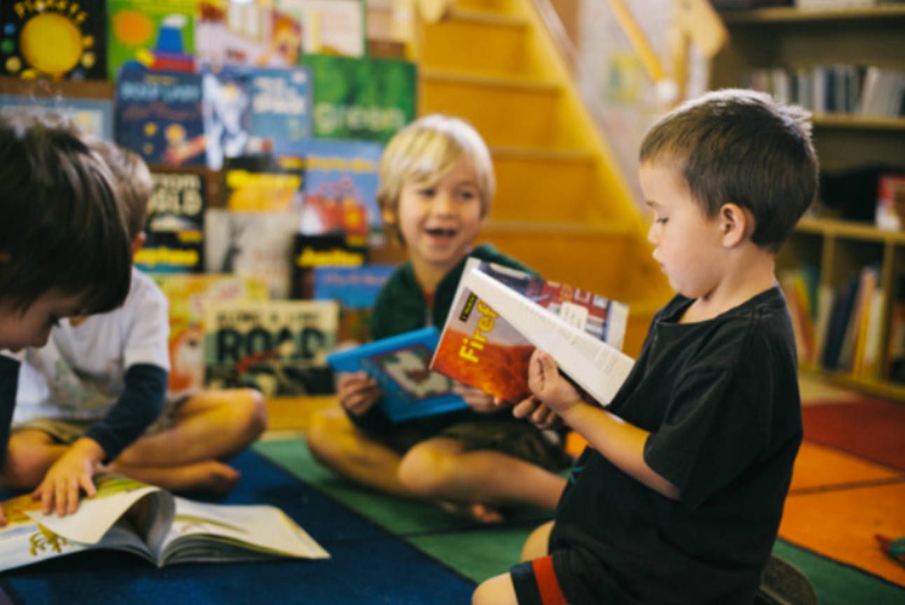 Three children sitting on the floor reading books in a classroom