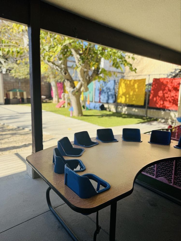 Empty classroom table with blue chairs facing an outdoor play area