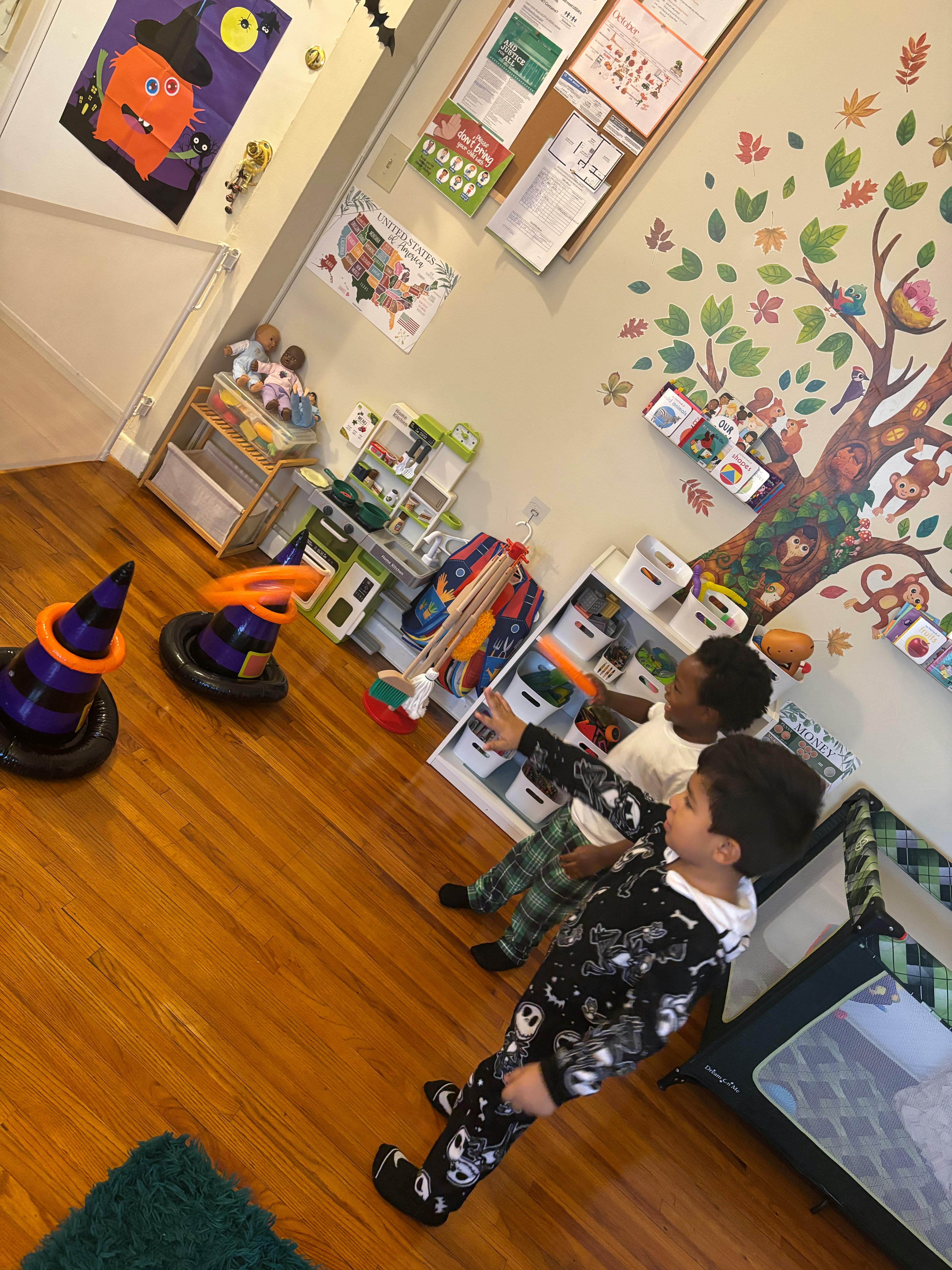 Two children playing in a room with toys and a tree mural