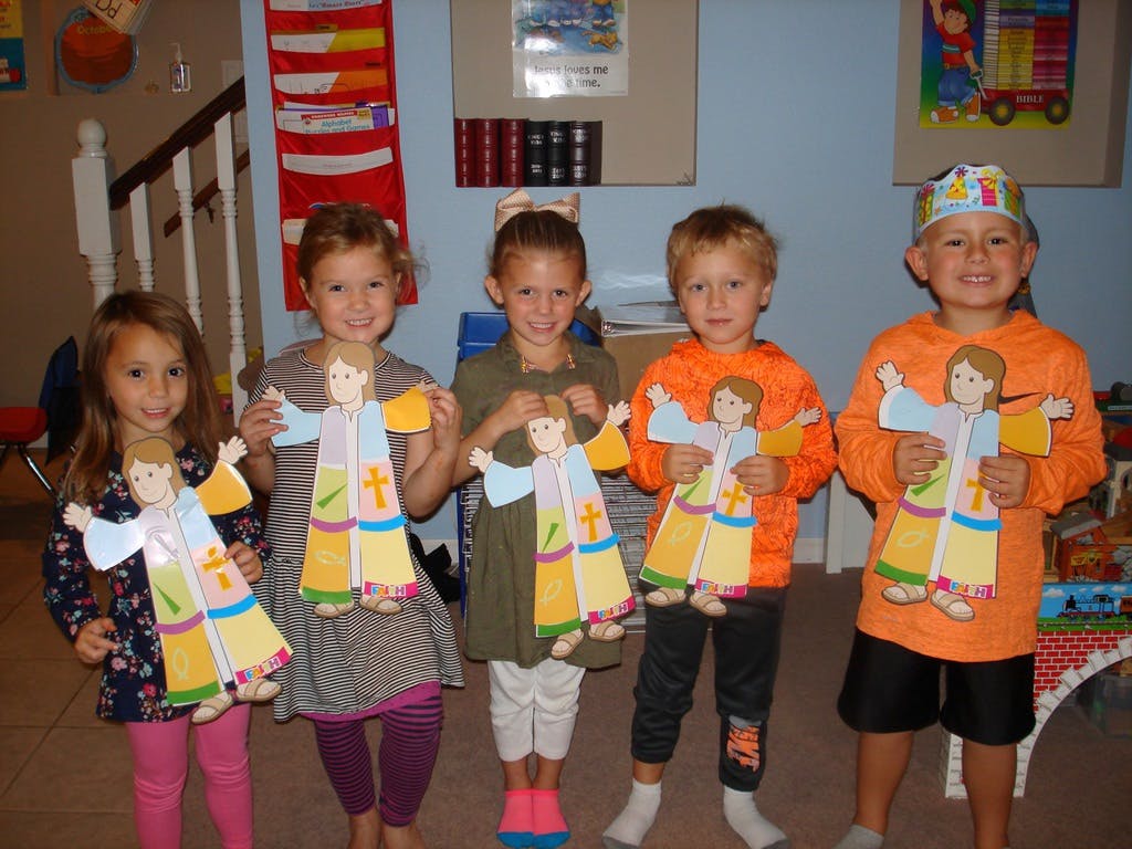 Five children holding up paper crafts of people in robes