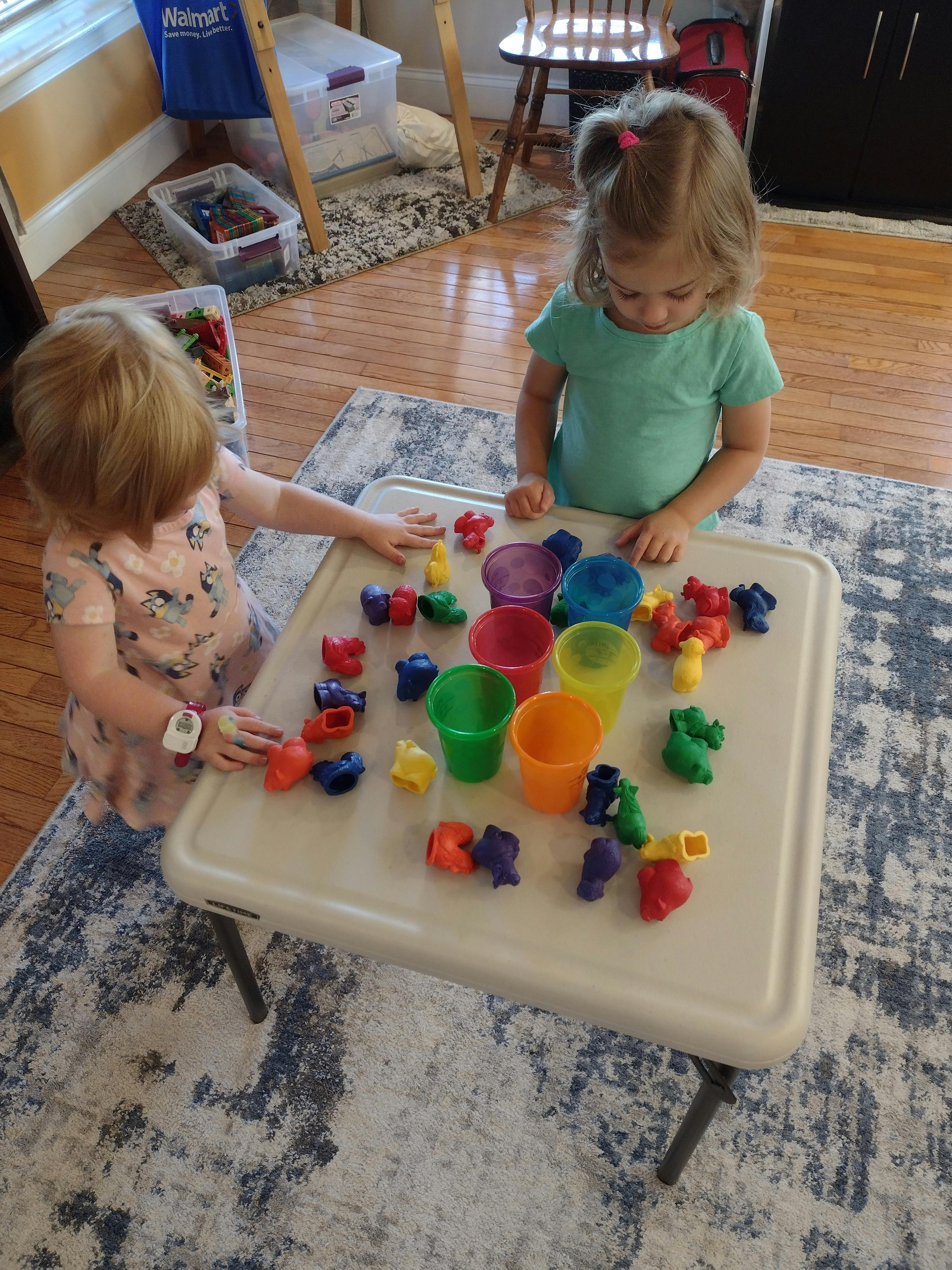 Two children playing with colorful cups and small toys on a table