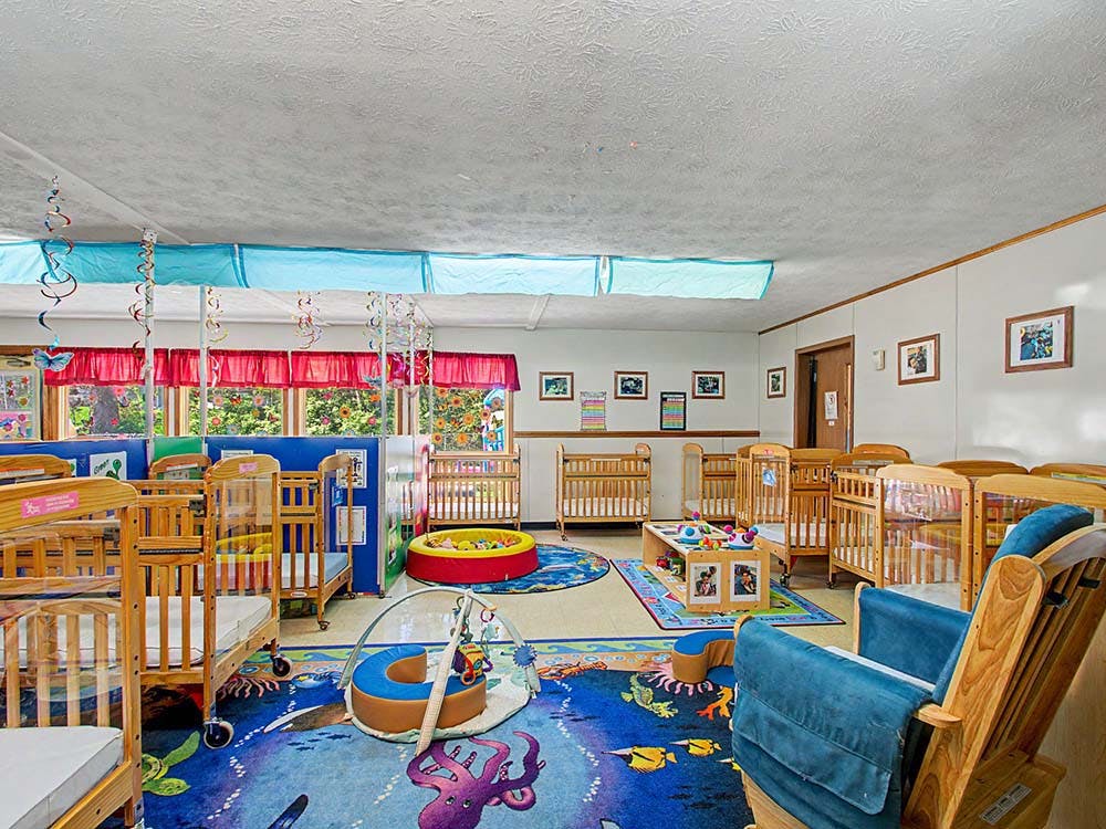 A daycare room with multiple cribs, an octopus rug, and a ball pit