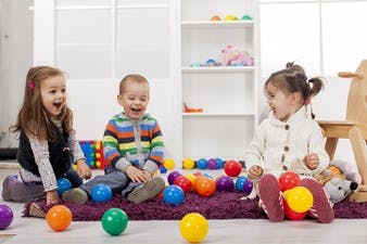 Three children playing with colorful balls on a rug