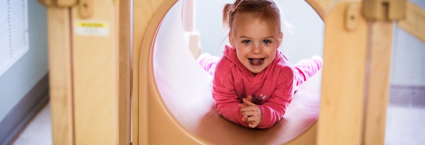 Child in pink shirt crawling through a wooden tunnel
