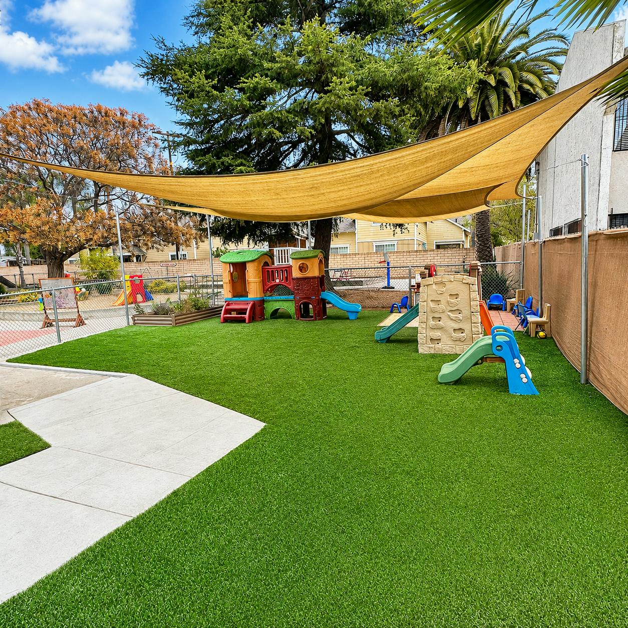 Playground equipment on artificial turf under a large shade sail