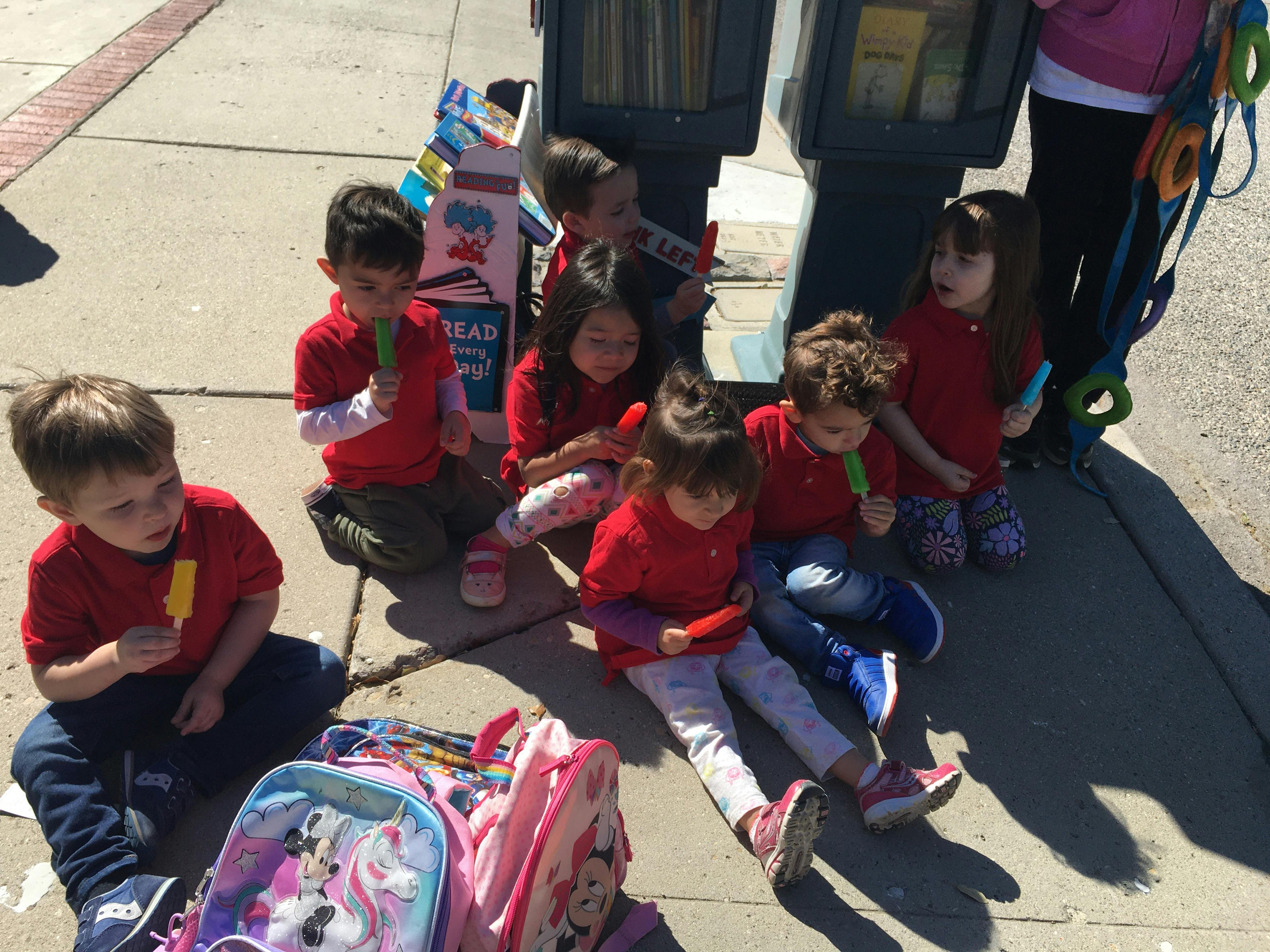 Group of children sitting on a sidewalk eating popsicles