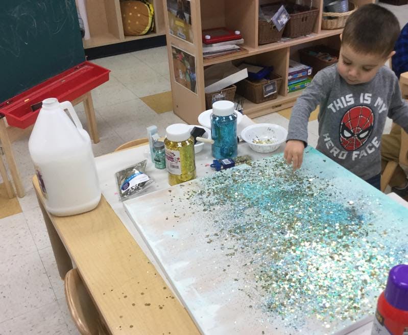 Child playing with glitter on a table in a classroom