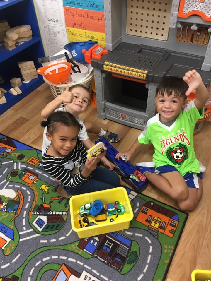 Three children playing with toy cars on a road map rug