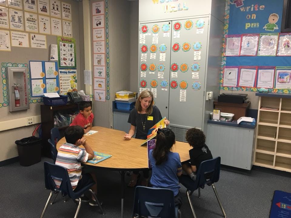 Person reading to children at a table in a classroom