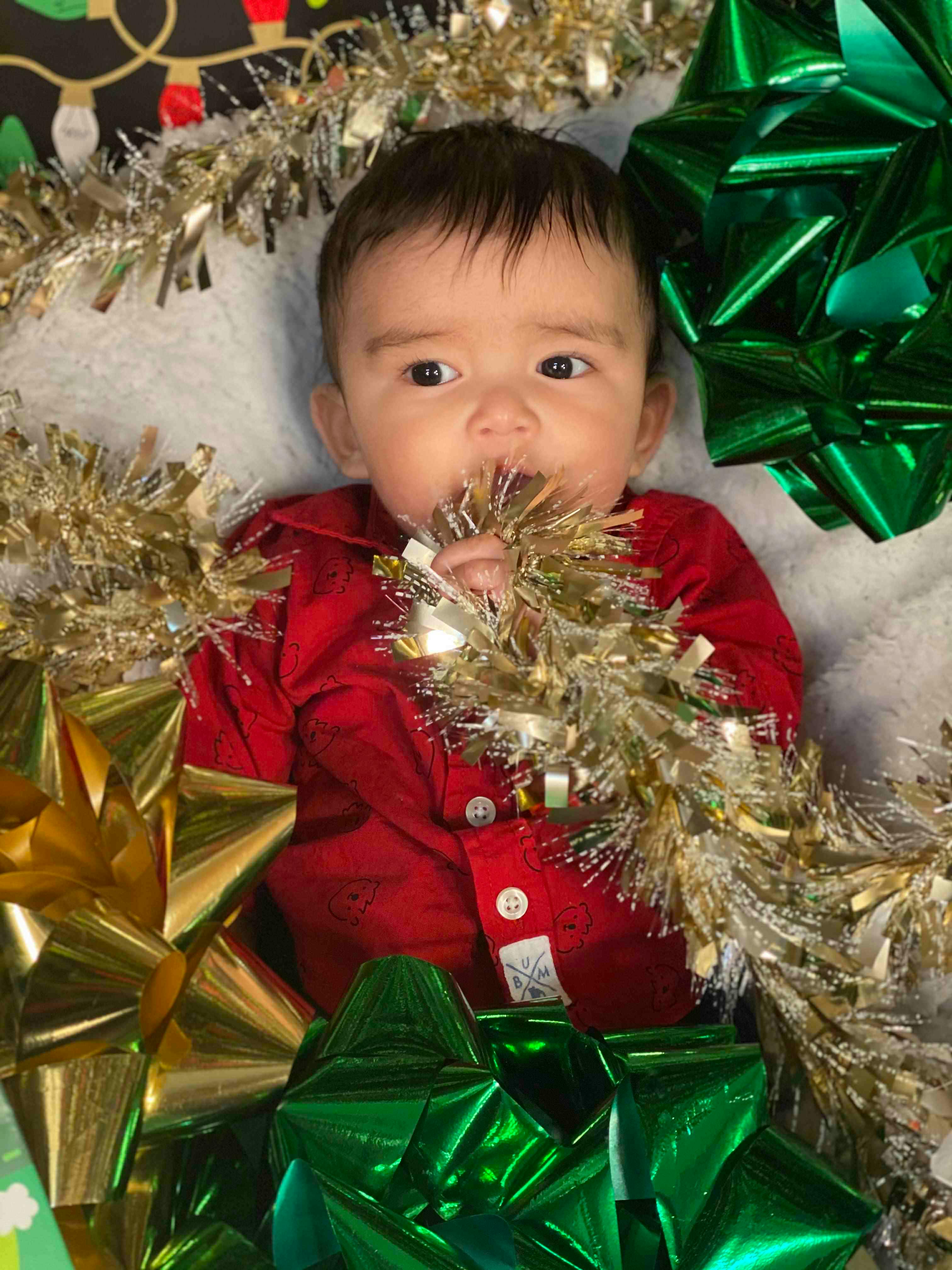 Child in red shirt holding tinsel in mouth surrounded by bows