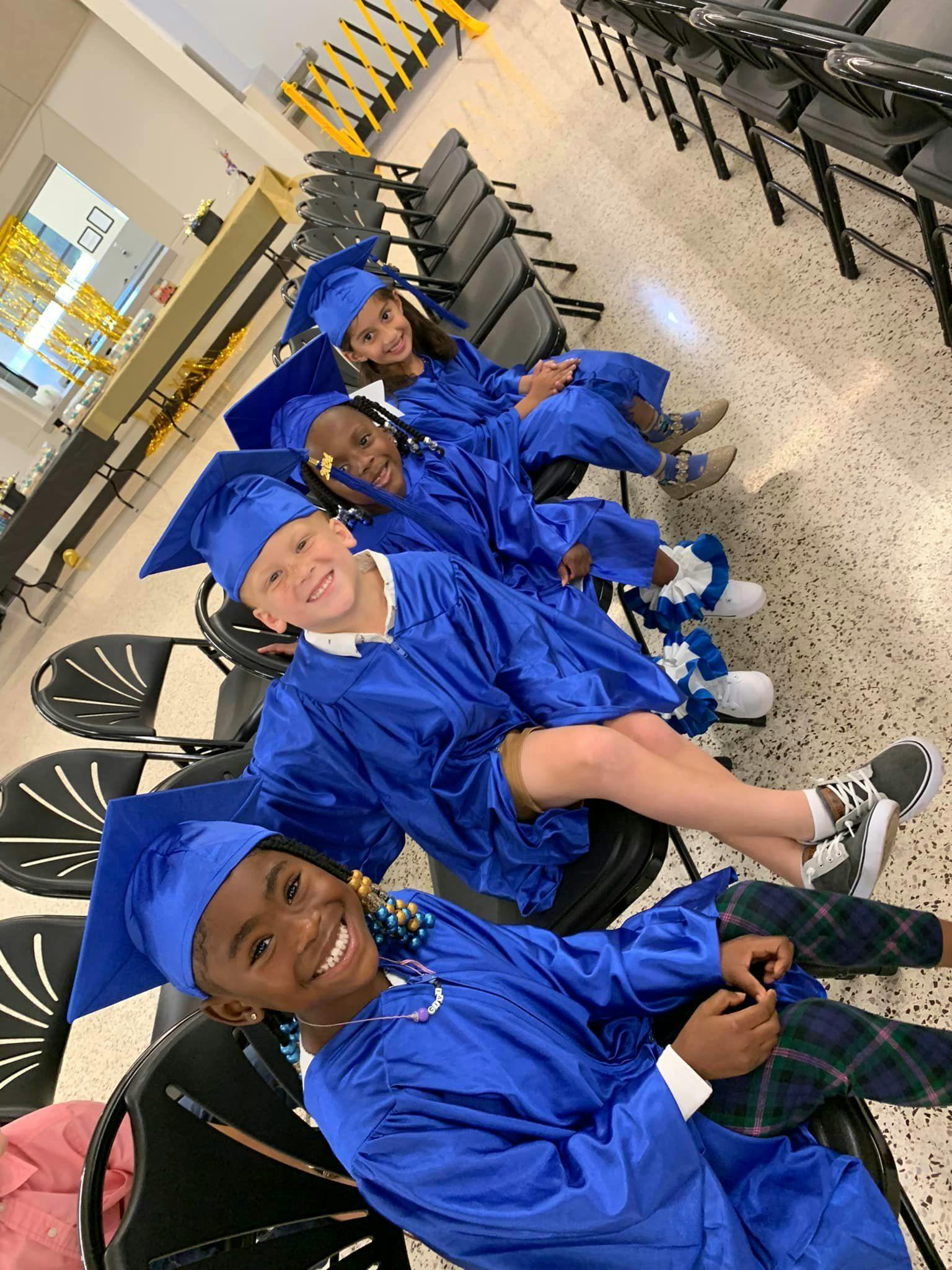 Five children in blue graduation caps and gowns sitting in chairs