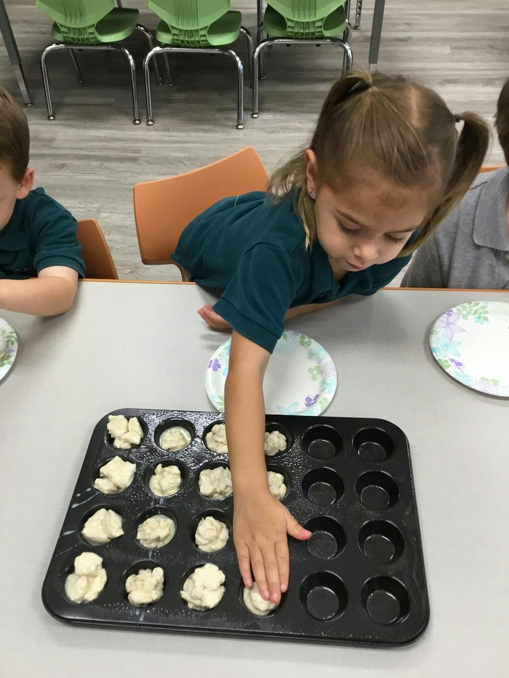 Child placing dough into a muffin tin