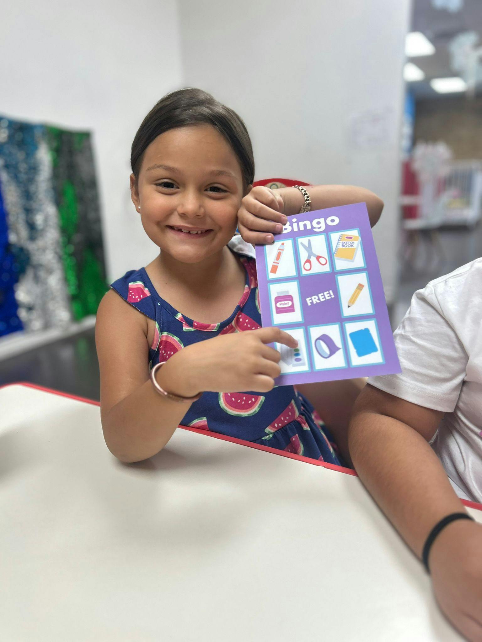 Child holding up a purple bingo card with school supplies