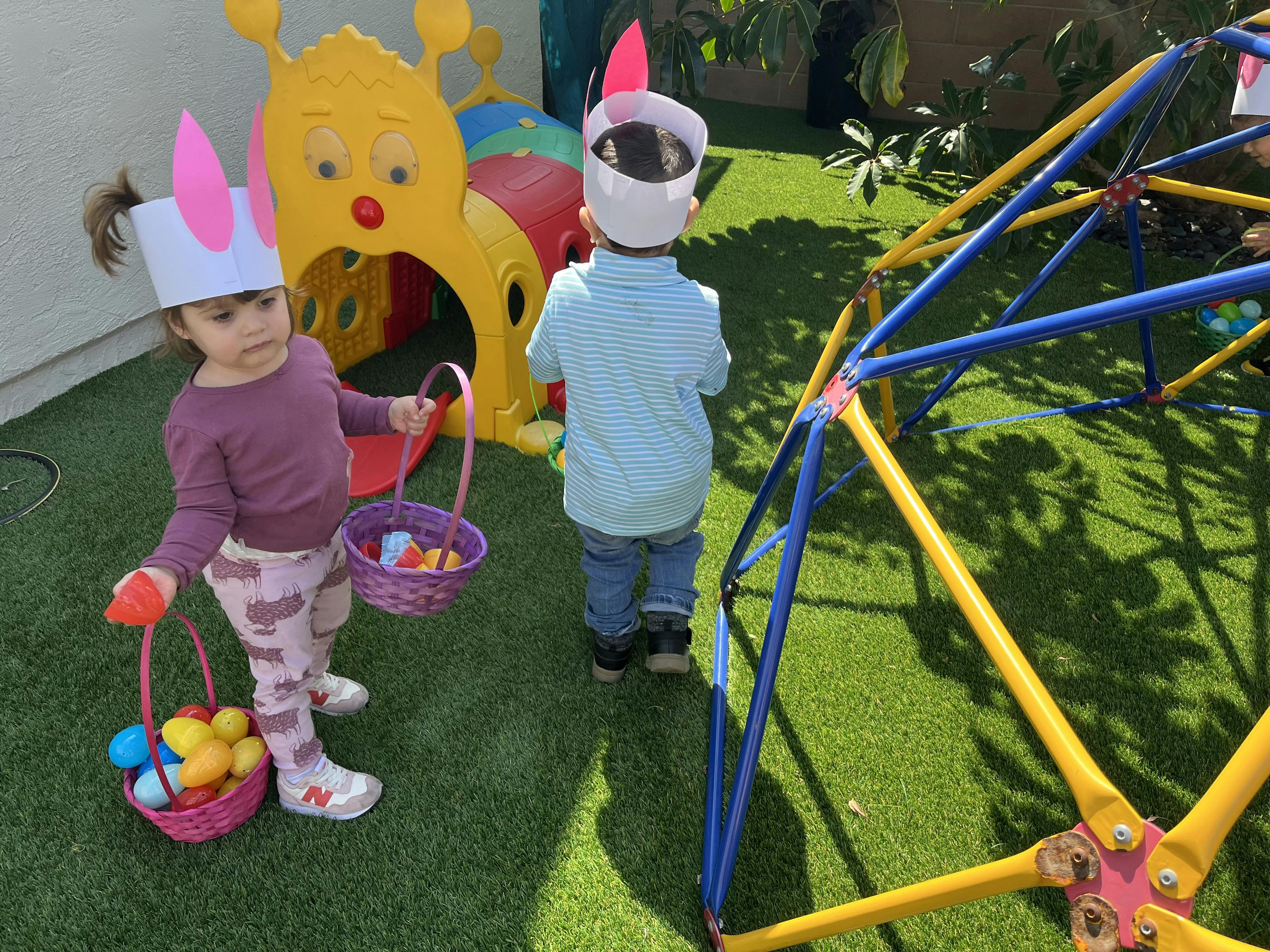 Two children wearing bunny ear headbands and holding baskets with eggs