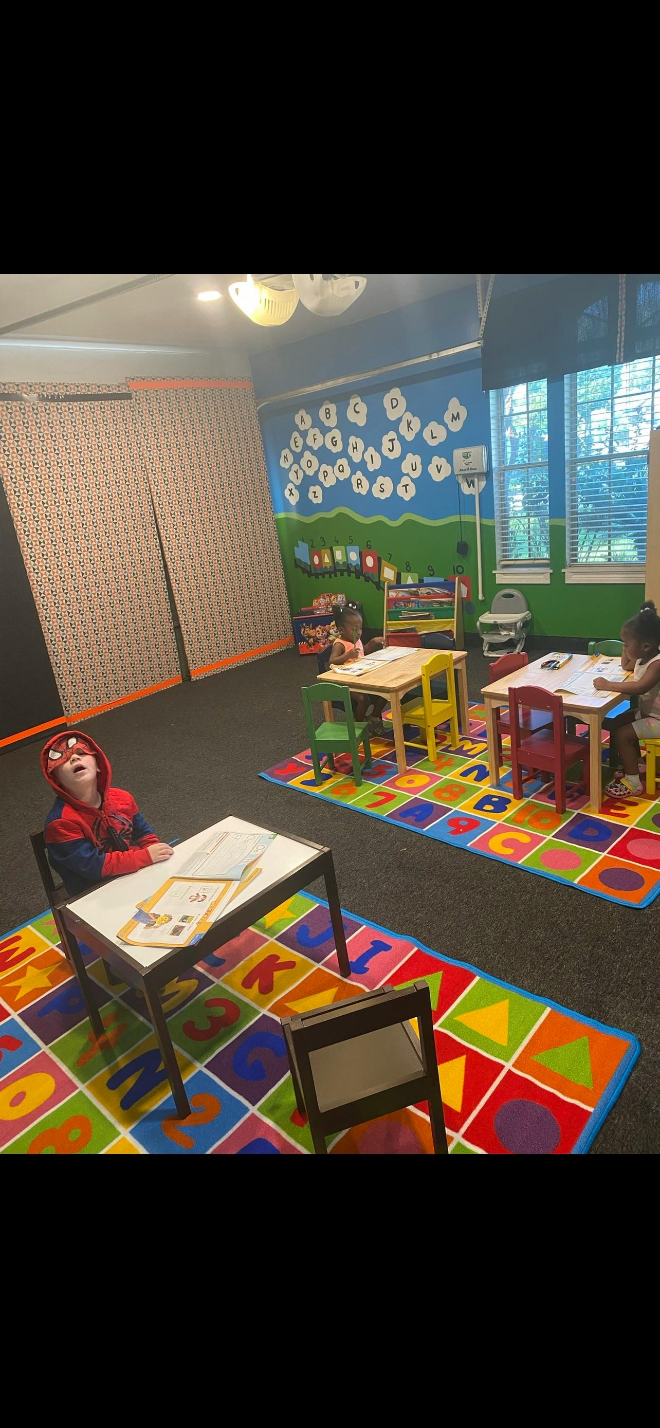 Child in a Spider-Man hoodie sitting at a small desk in a classroom
