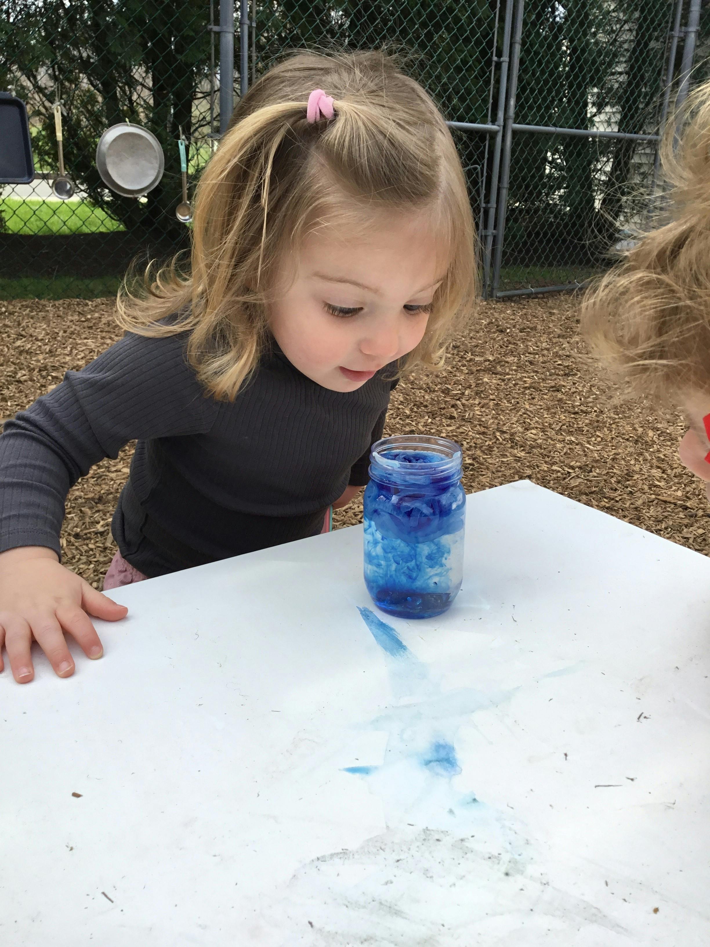 Child looking at a jar with blue liquid on a white surface
