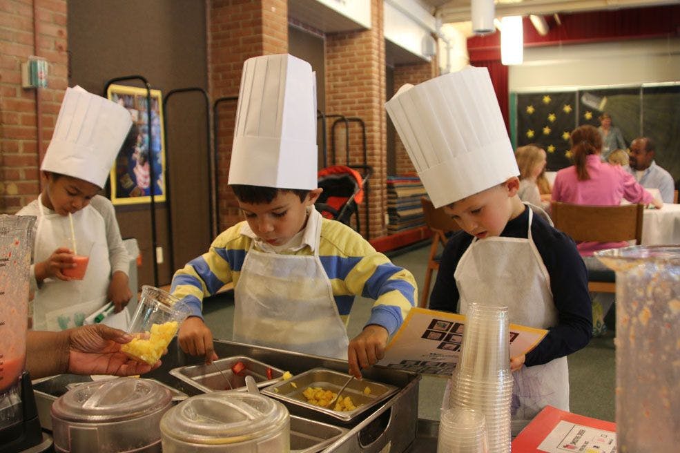 Children in chef hats and aprons preparing food