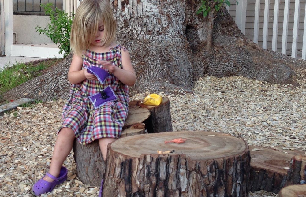 Child sitting on a tree stump and holding purple objects