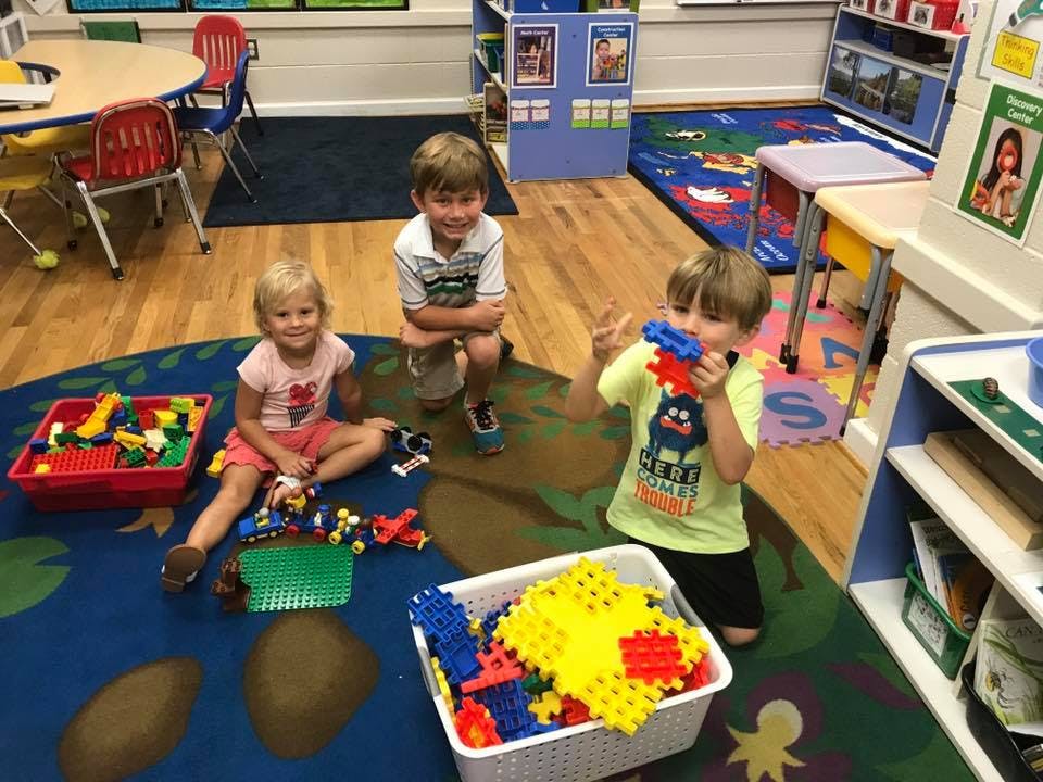 Three children playing with building blocks on a rug
