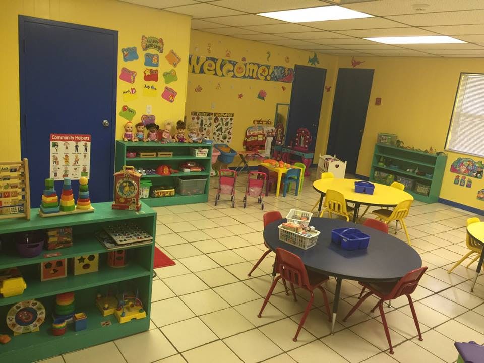 A classroom with small tables and chairs, shelves with toys, and a "Welcome" sign
