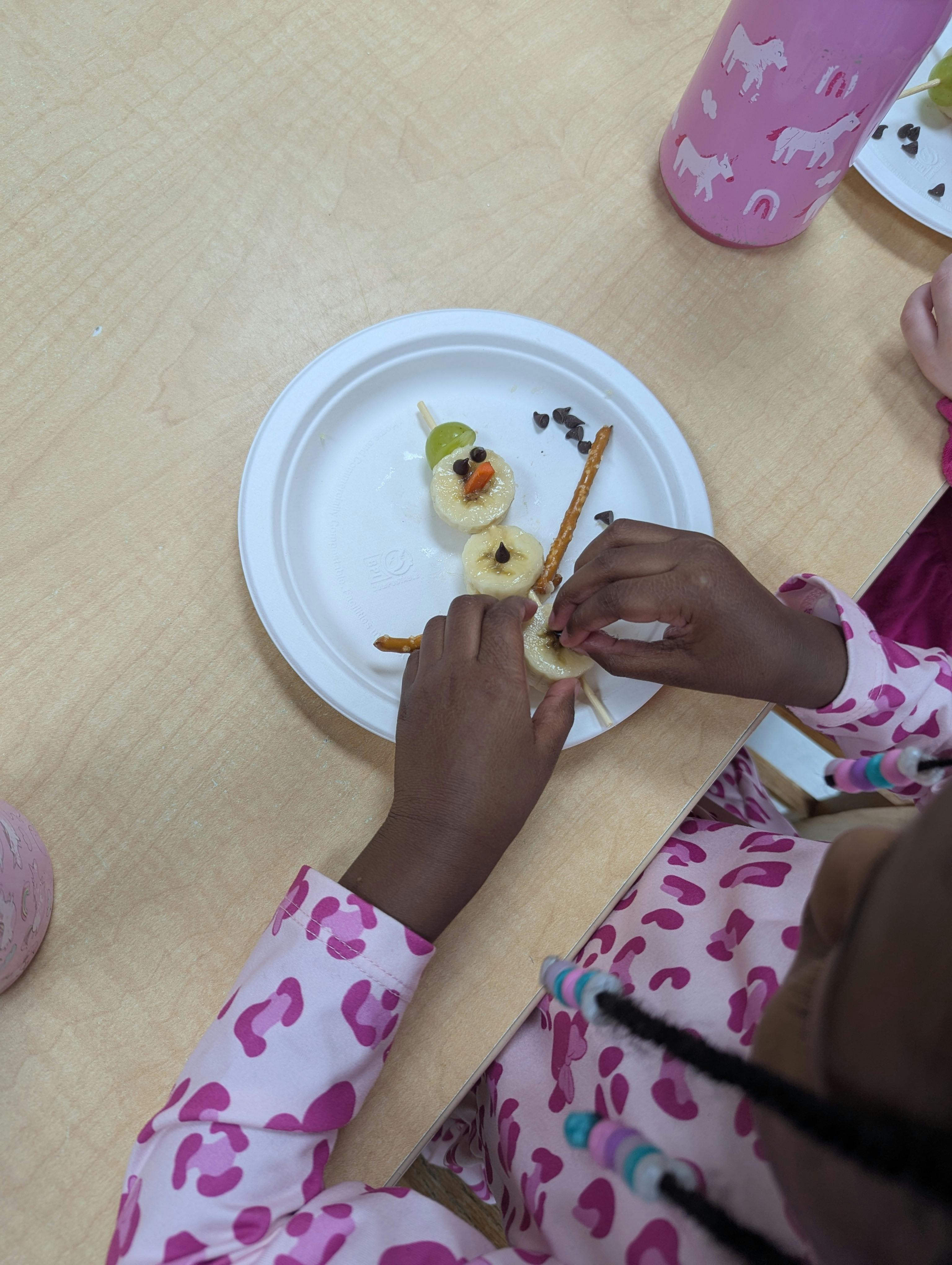 Child making a banana and pretzel snowman on a paper plate