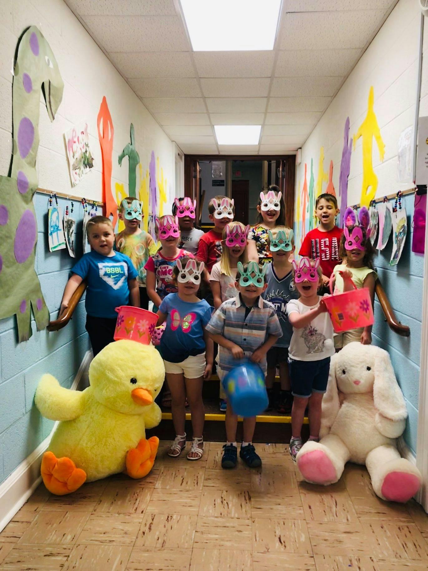 Children wearing animal masks and holding baskets in a hallway