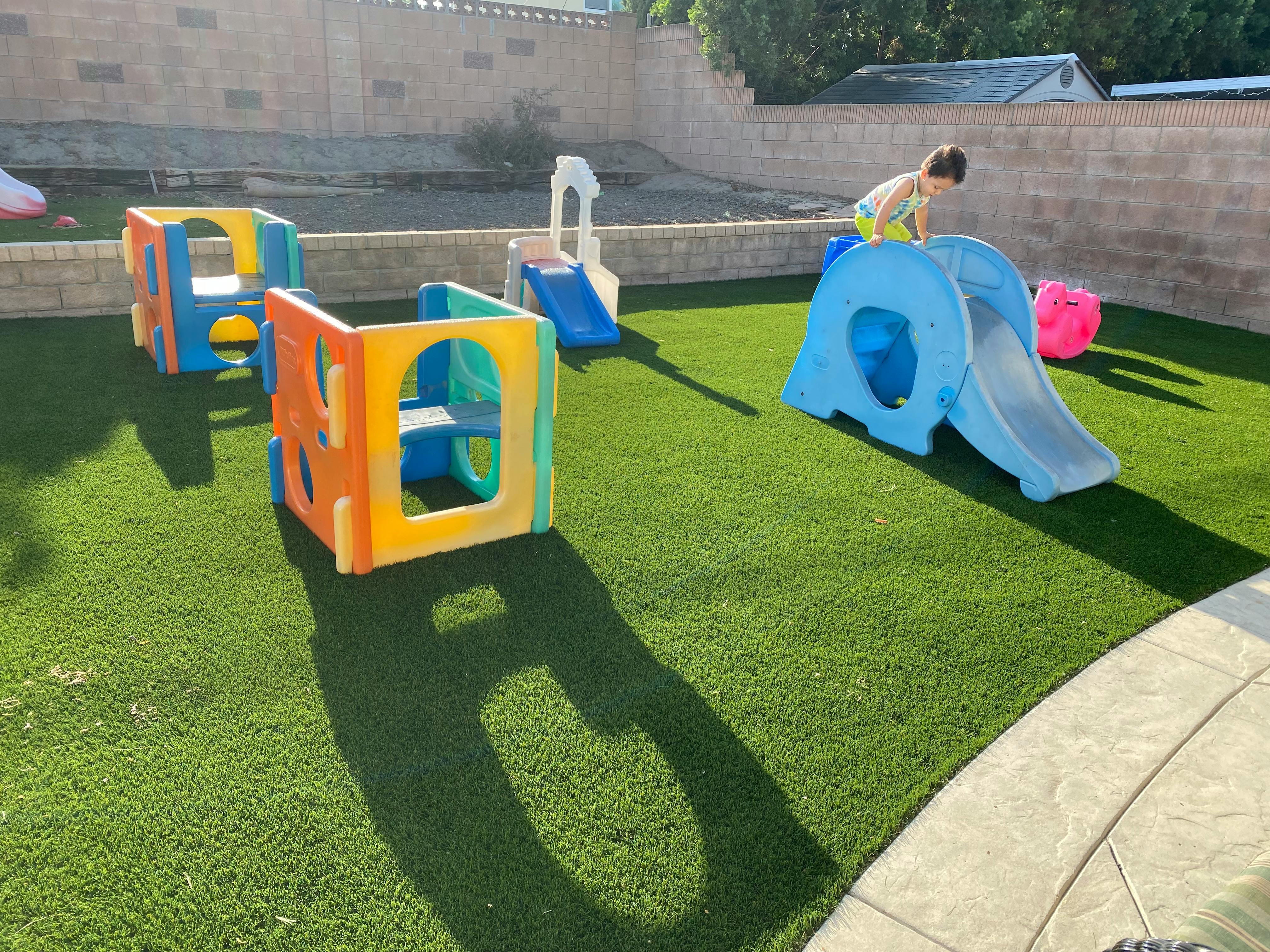 Child on a blue slide on artificial grass with play structures