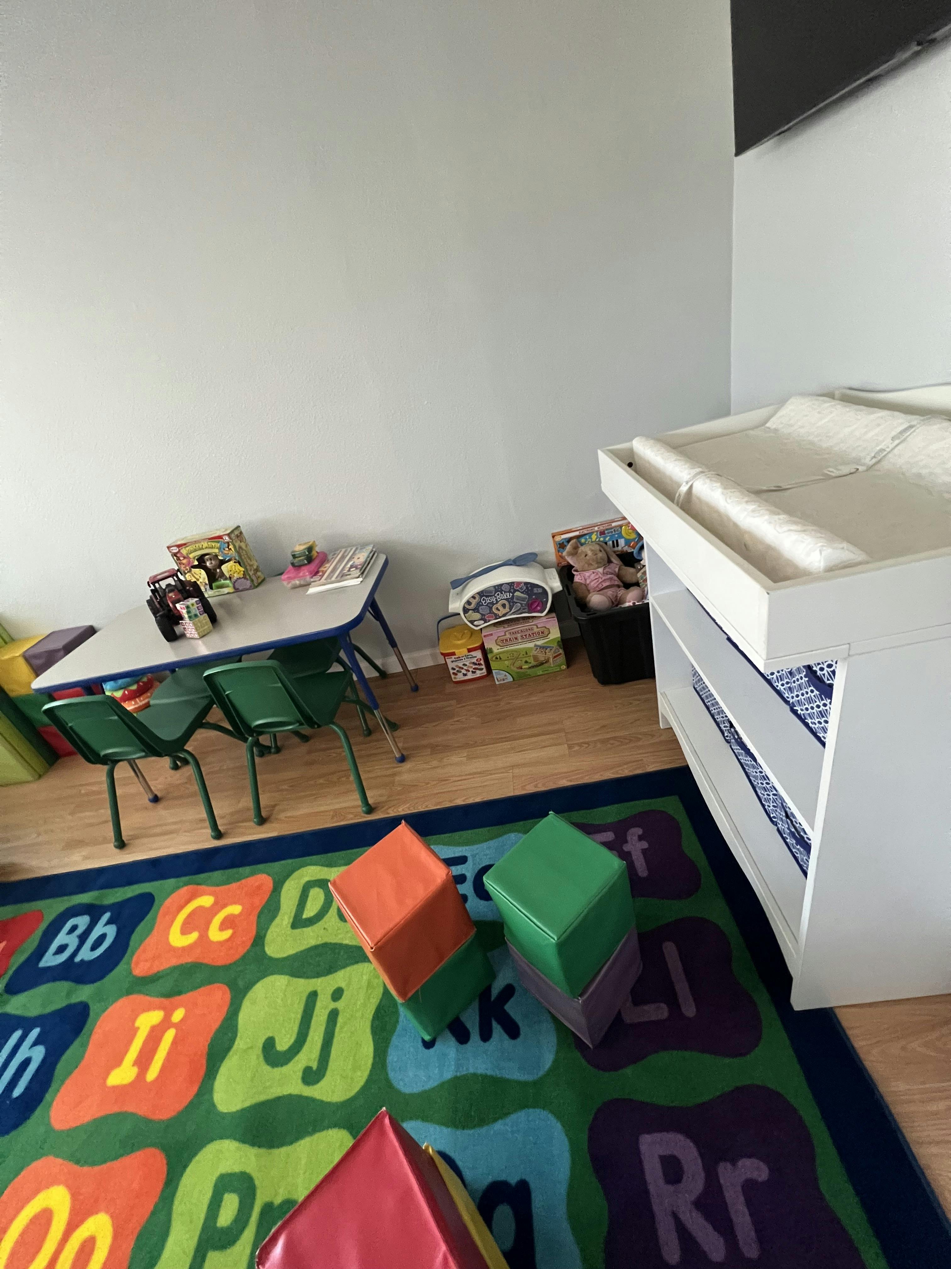 Classroom or play area with a child-sized table, chairs, changing table, and alphabet rug