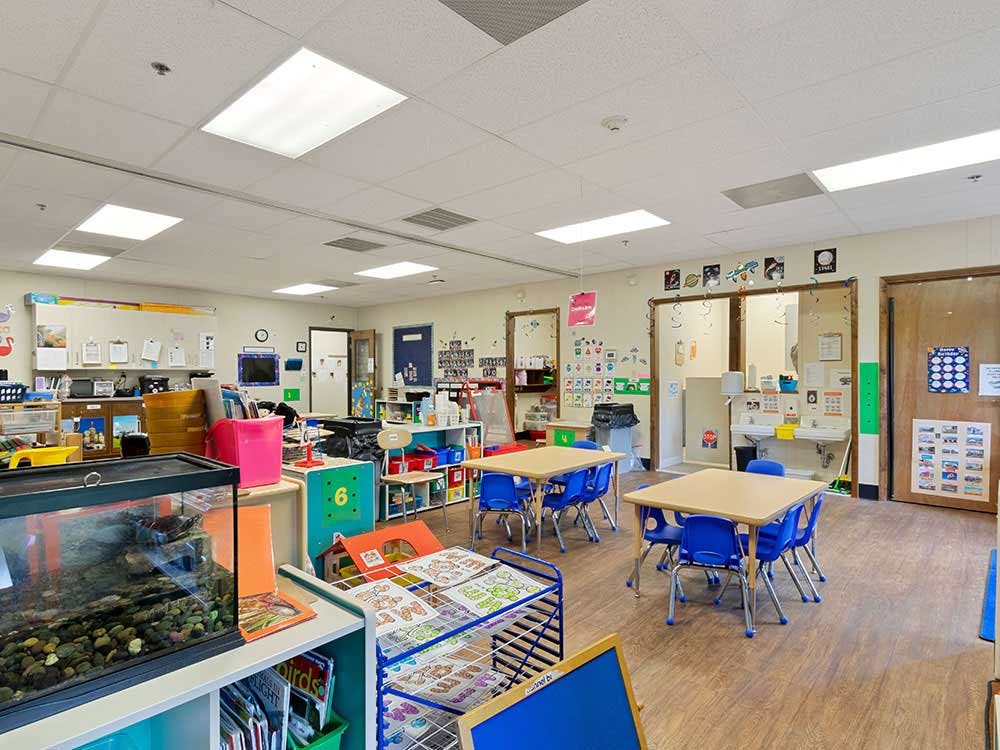 Empty classroom with small tables and chairs, shelves, and a large fish tank