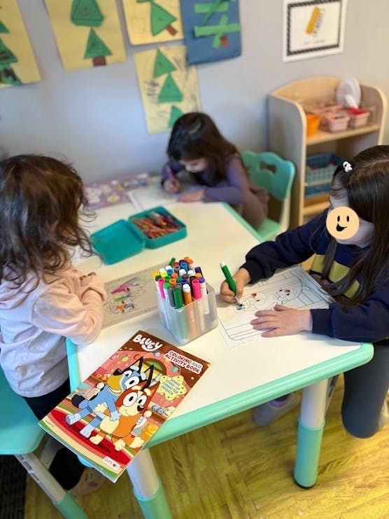 Three children coloring in a Bluey activity book at a small table