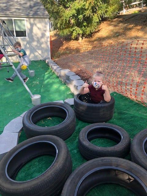 Child in a face mask sitting in a tire, another child on a ladder