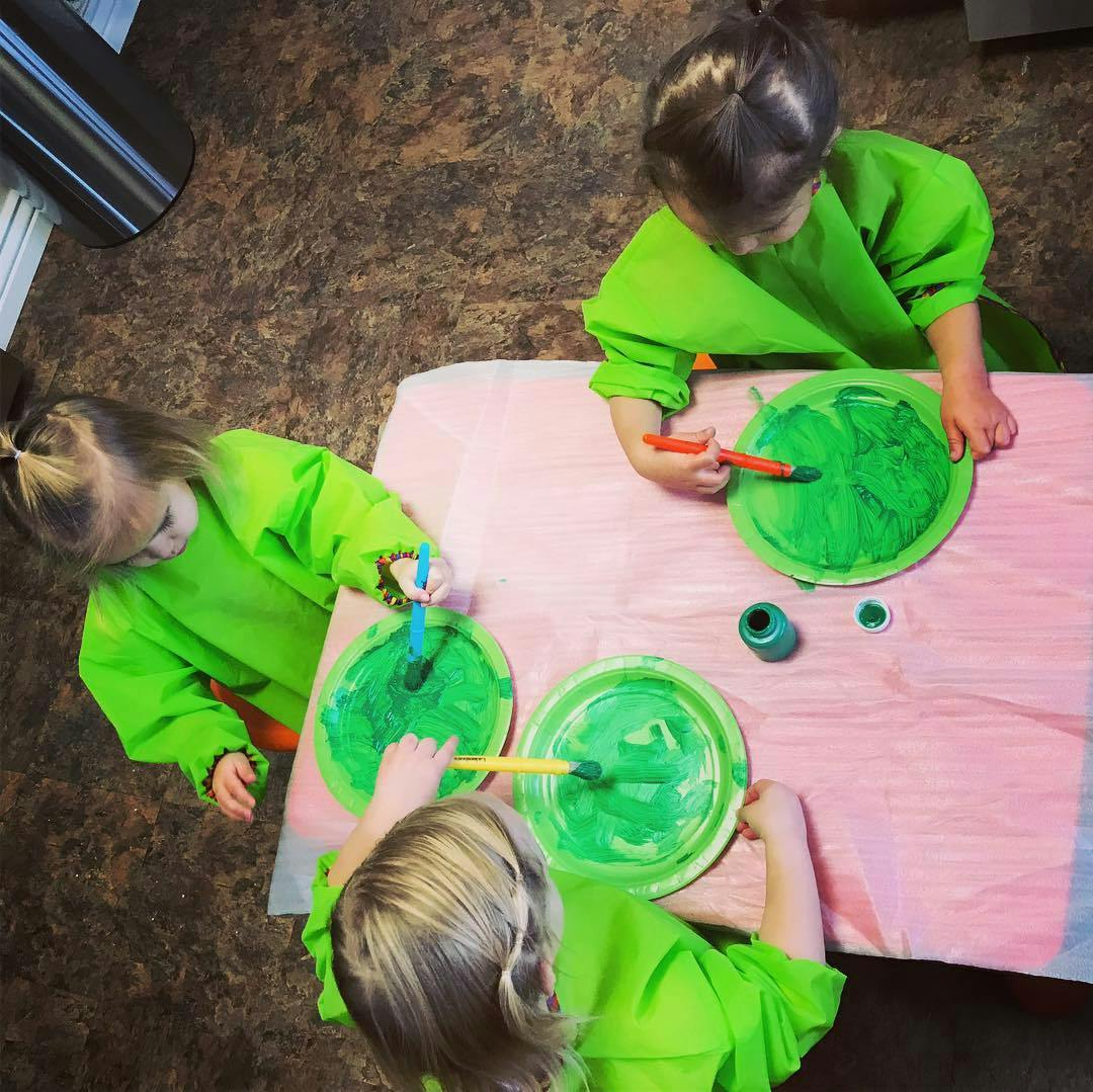 Three children painting green circles on paper plates