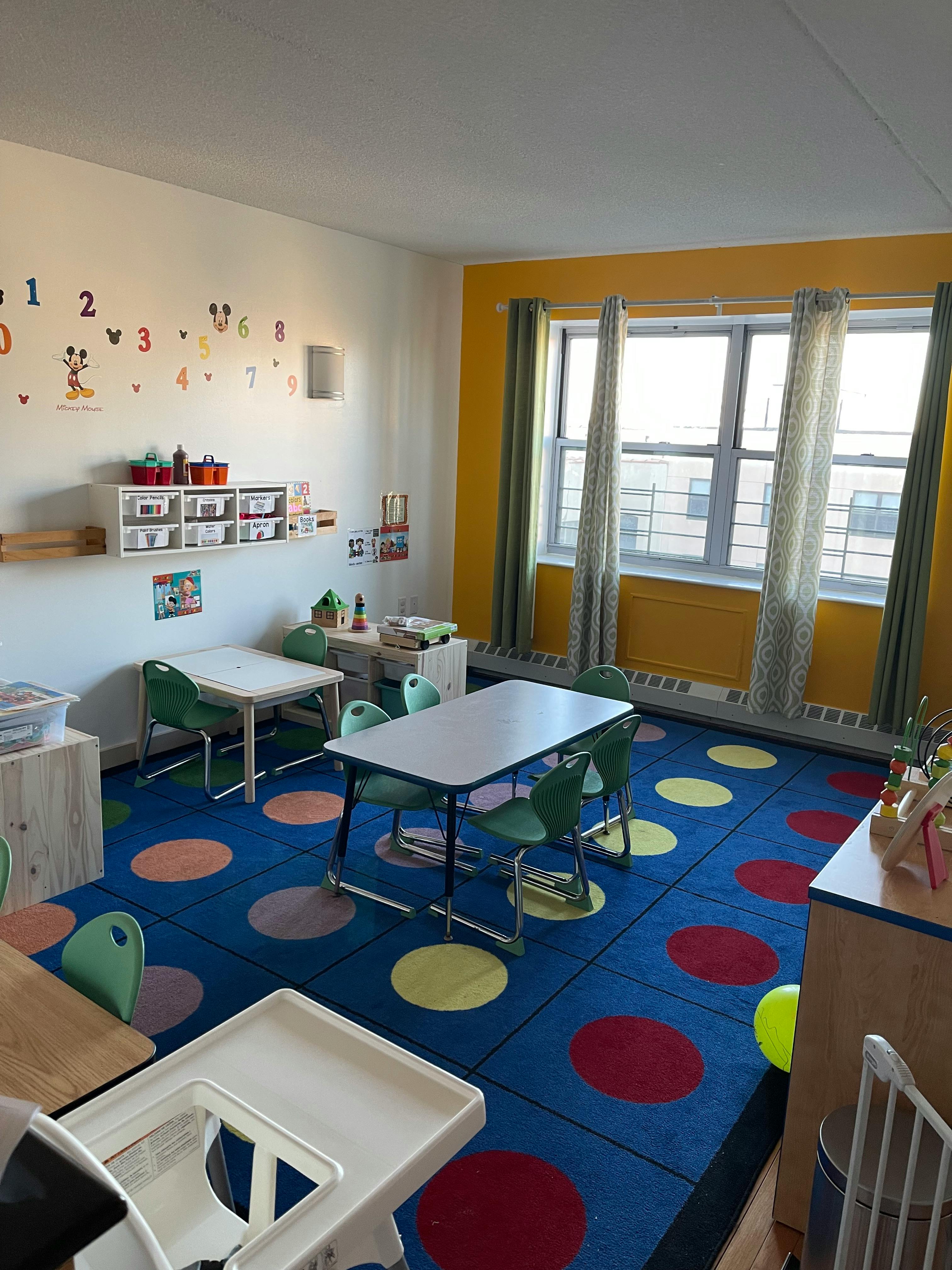 Classroom with small tables and chairs, colorful rug, and windows