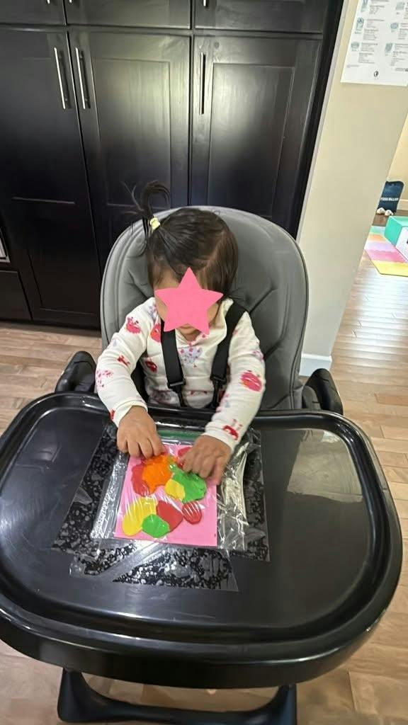 Child sitting in a high chair playing with paint in a sealed plastic bag