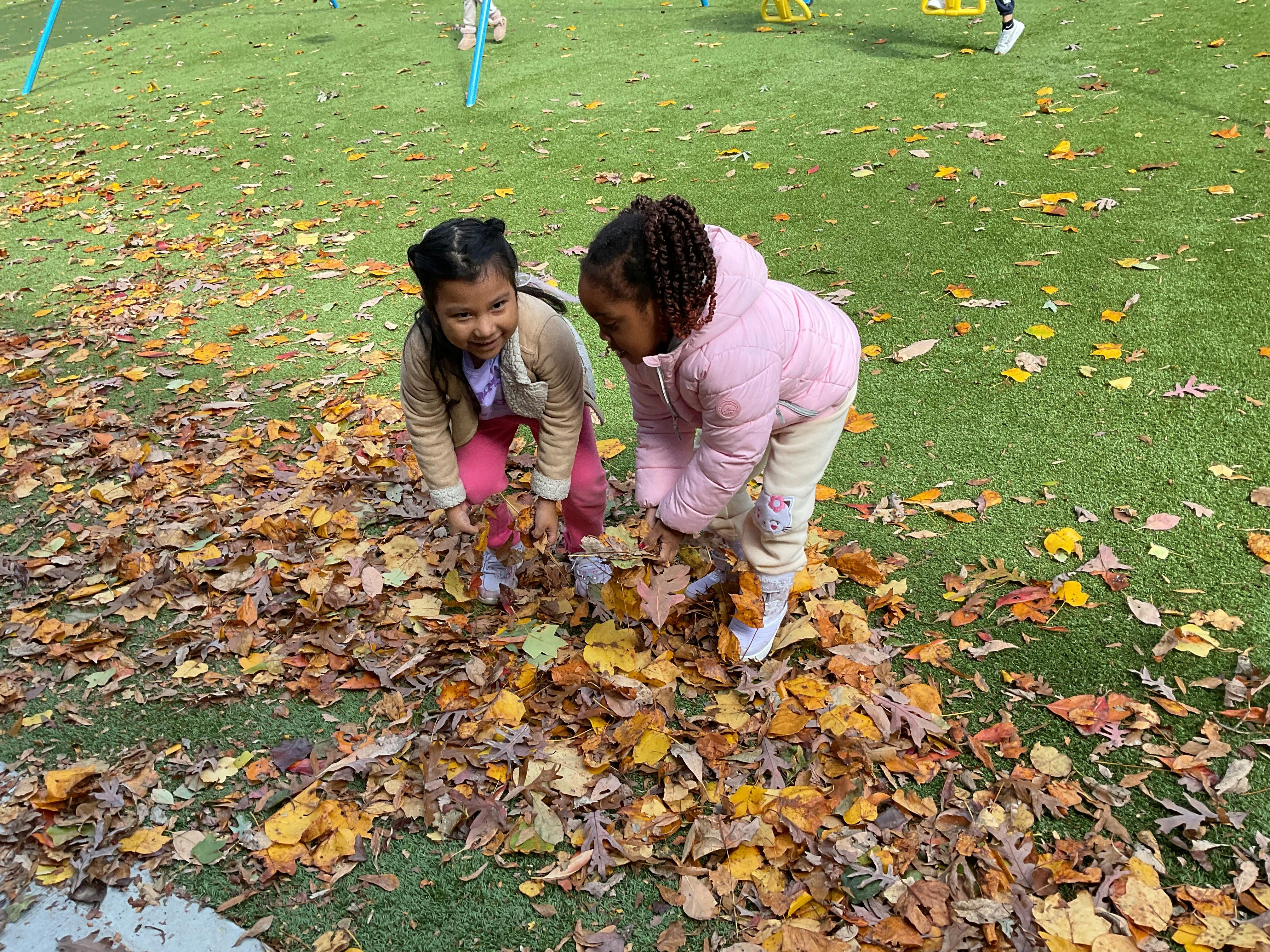 Two children bending down to gather autumn leaves on green turf