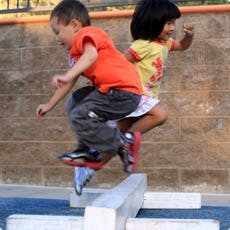 Two children jumping over a low obstacle