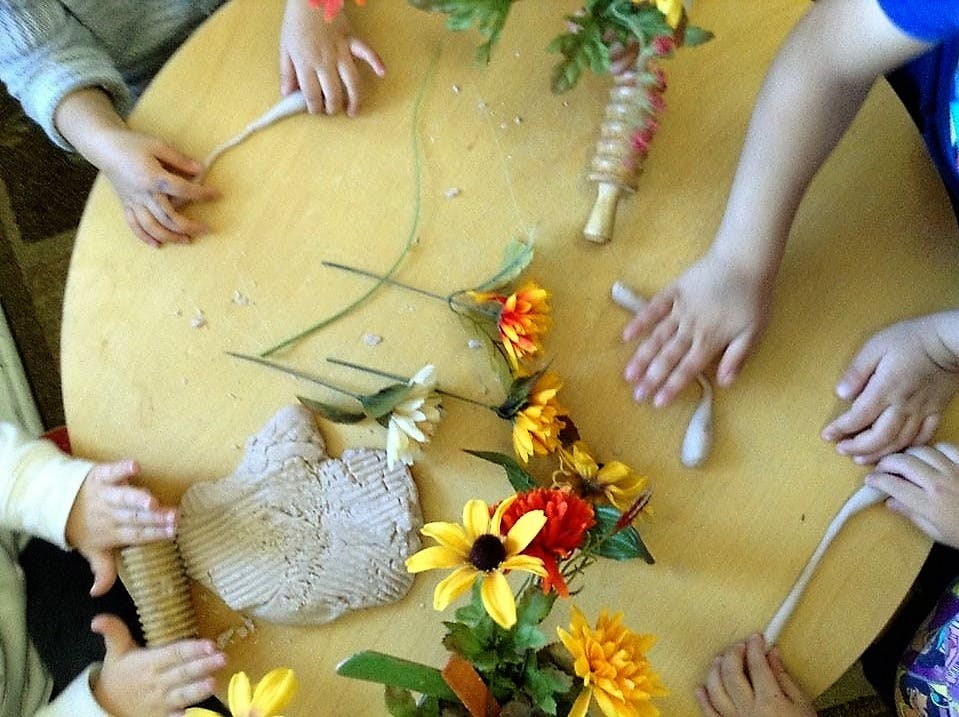 Children's hands working with clay and flowers on a round table
