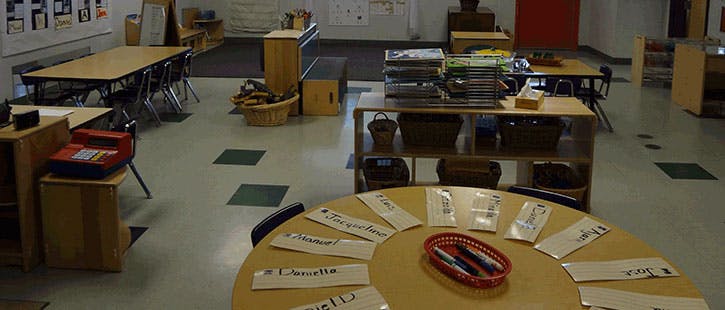Classroom with tables and chairs, shelves with items