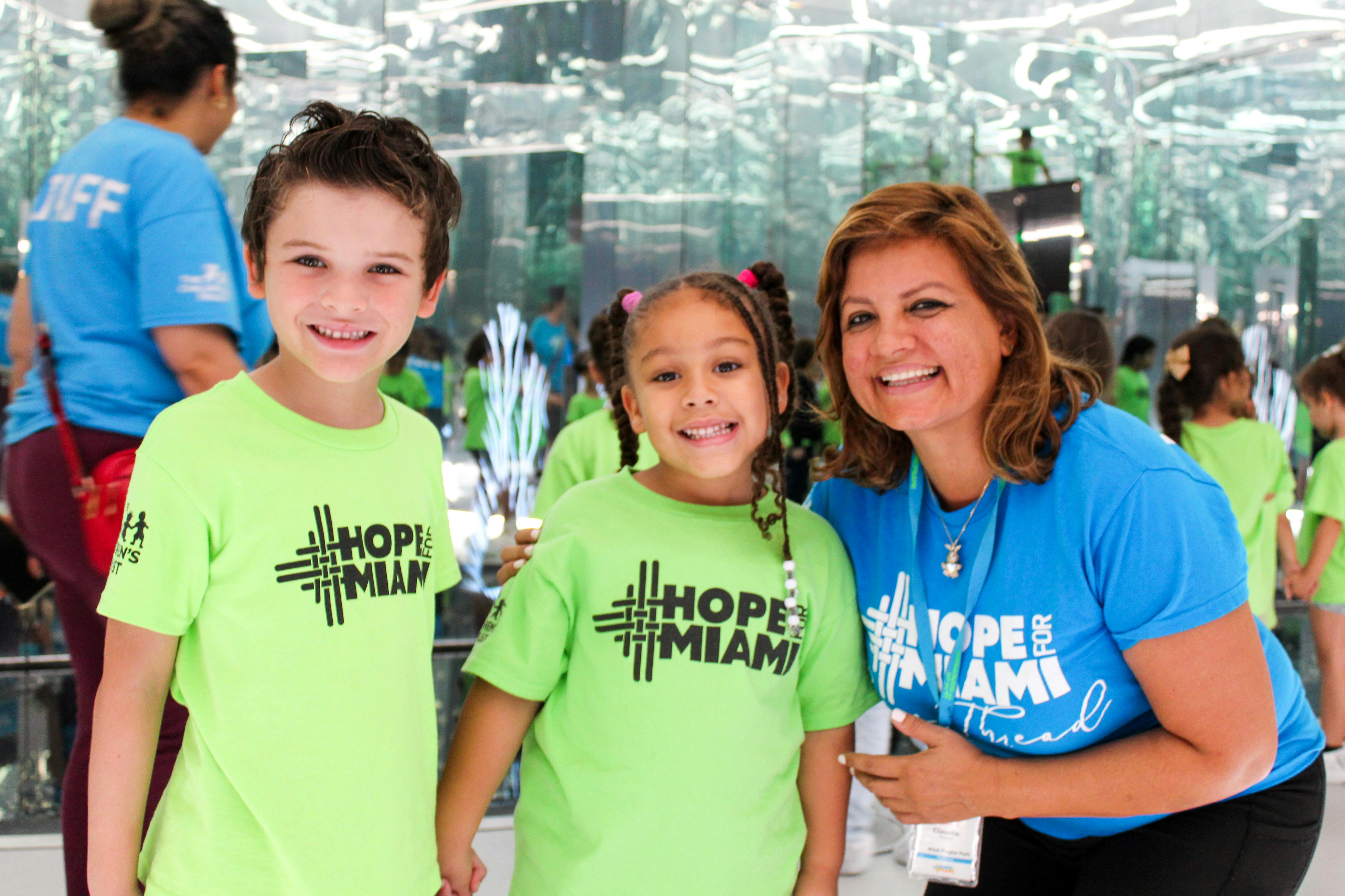 A person and two children wearing Hope for Miami t-shirts smiling