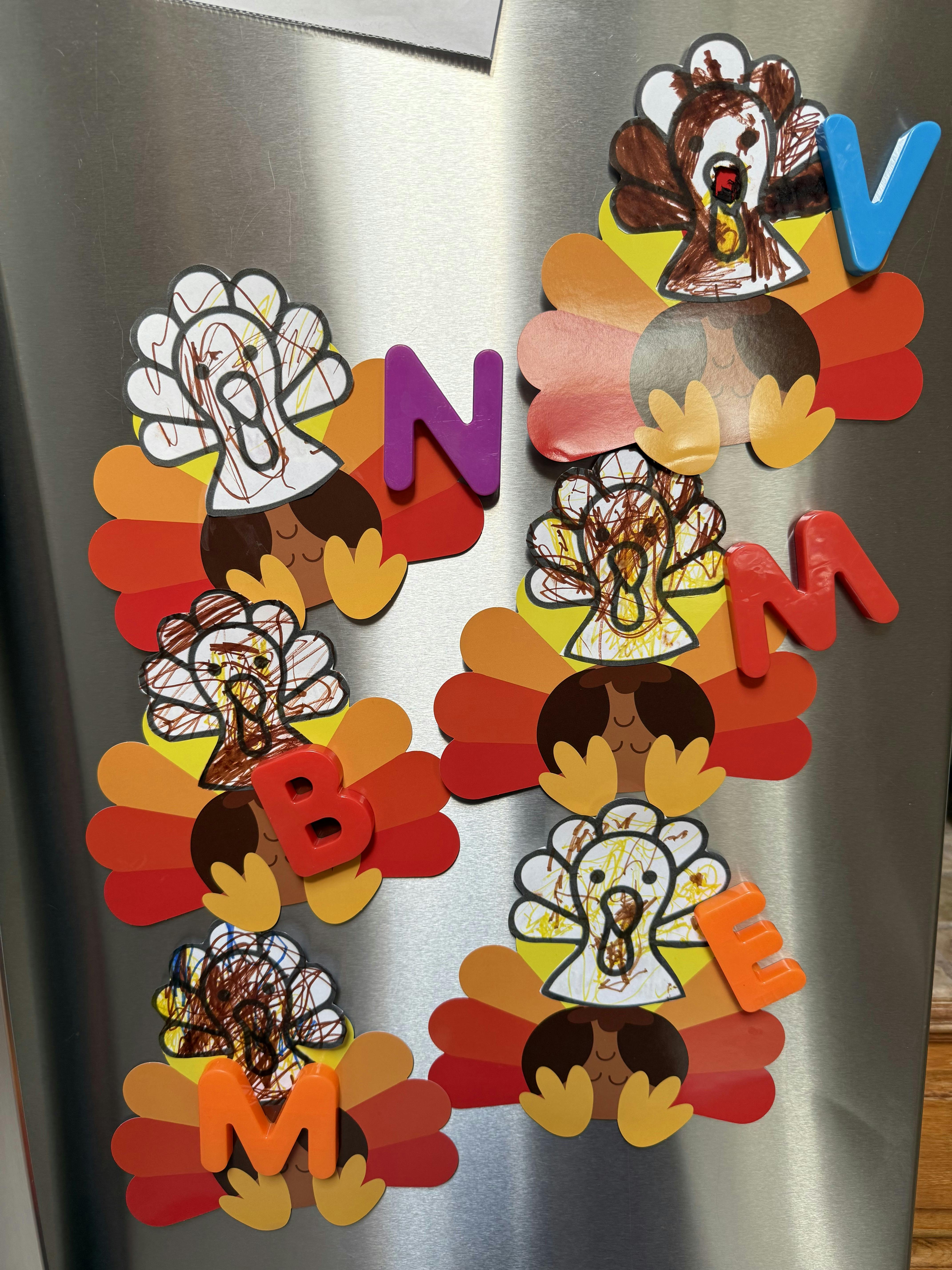 Child's turkey drawings and alphabet magnets on a stainless steel refrigerator