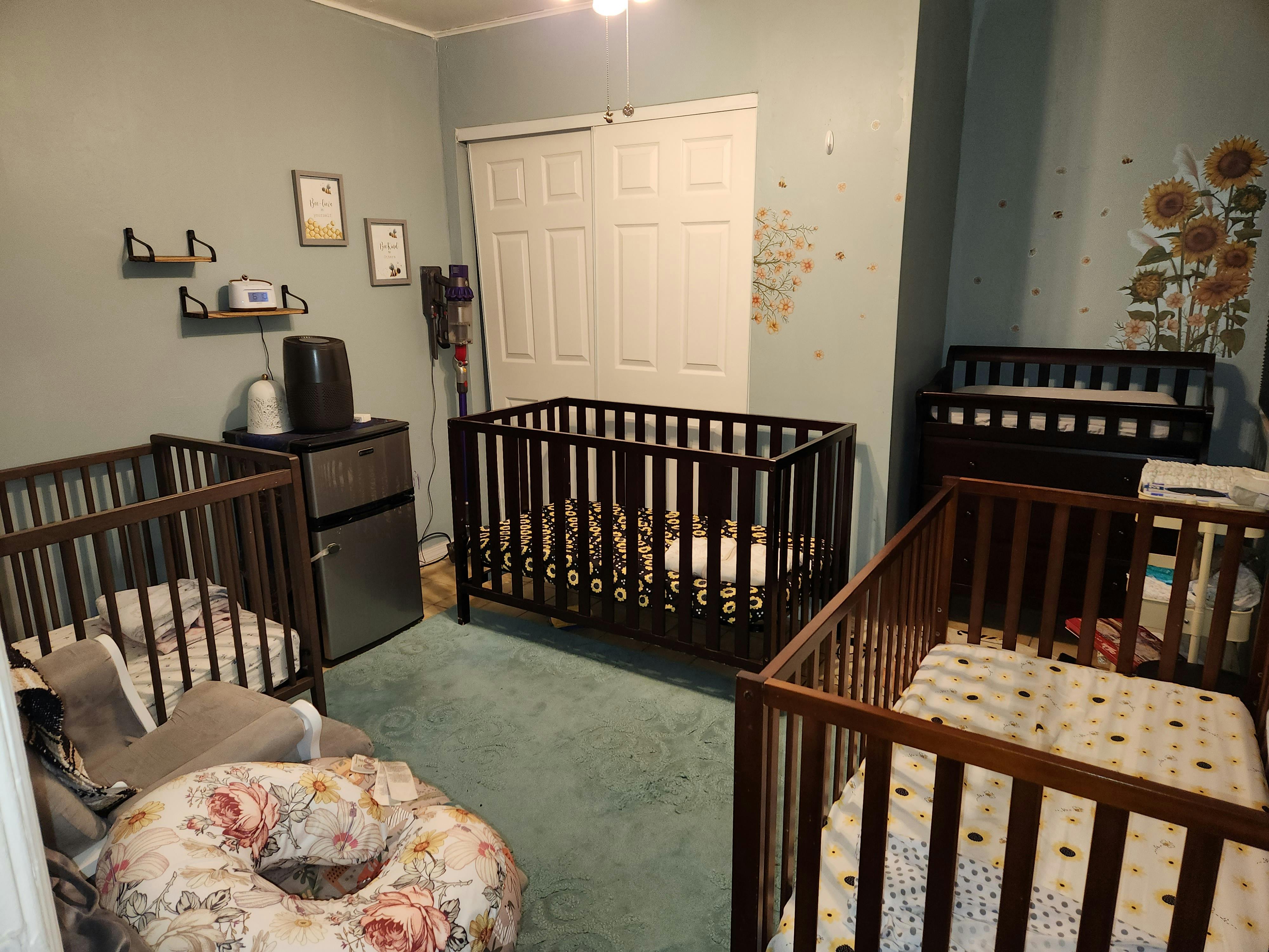Three cribs in a room with a mini-fridge and changing table